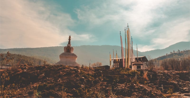 Scenic view of a small chorten with fluttering prayer flags beside a traditional Bhutanese house in a serene village setting